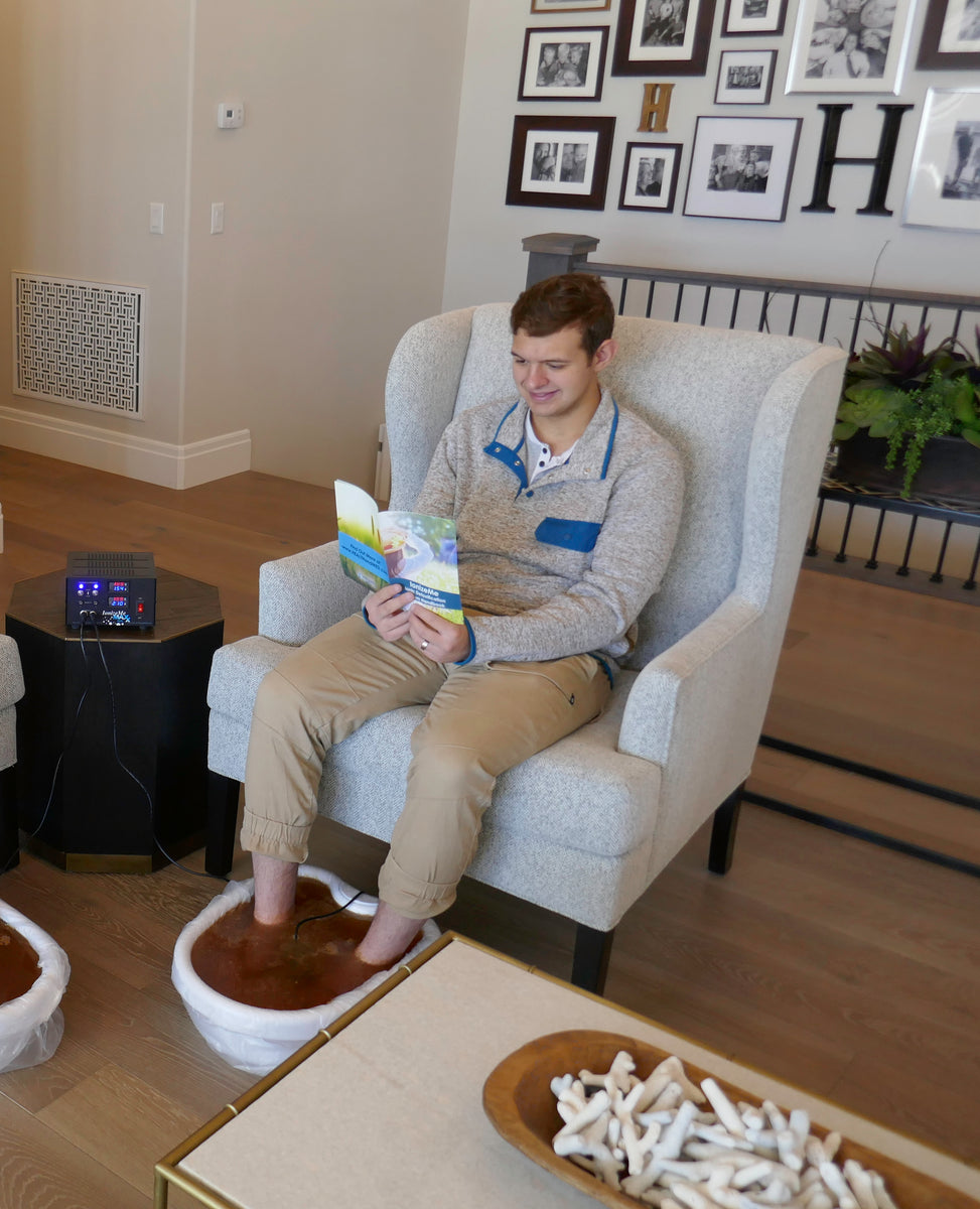 Man sitting in a chair holding a brochure doing an ionic foot detox with the IonizeMe Maxx Dual system