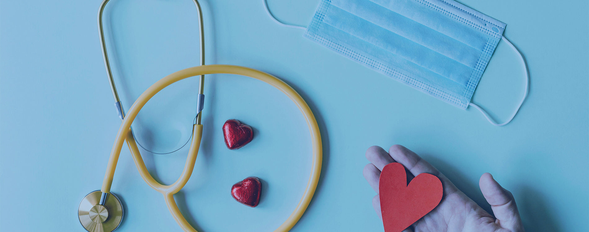 Stethescope, a mask and a hand holding a paper heart