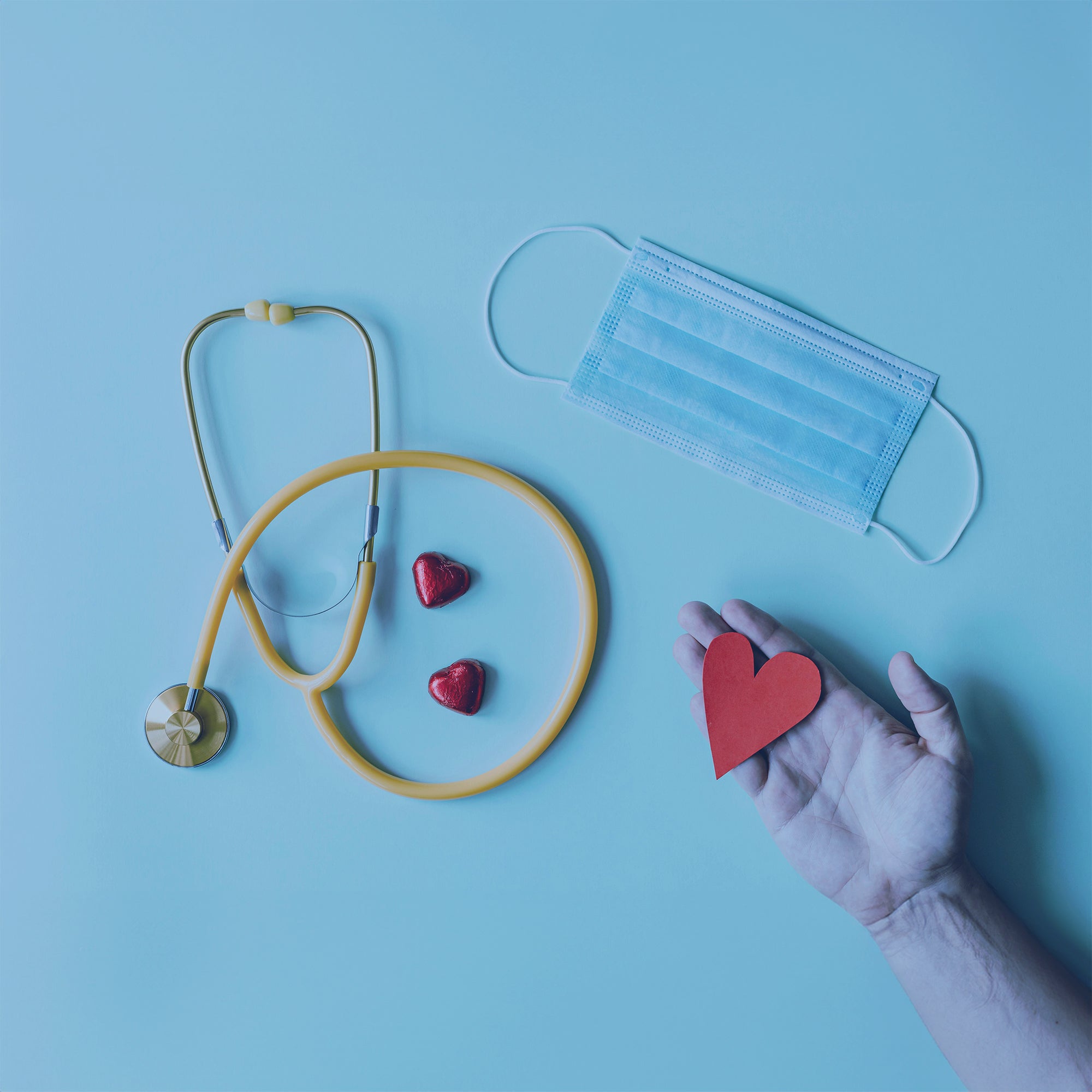 Stethescope, a mask and a hand holding a paper heart