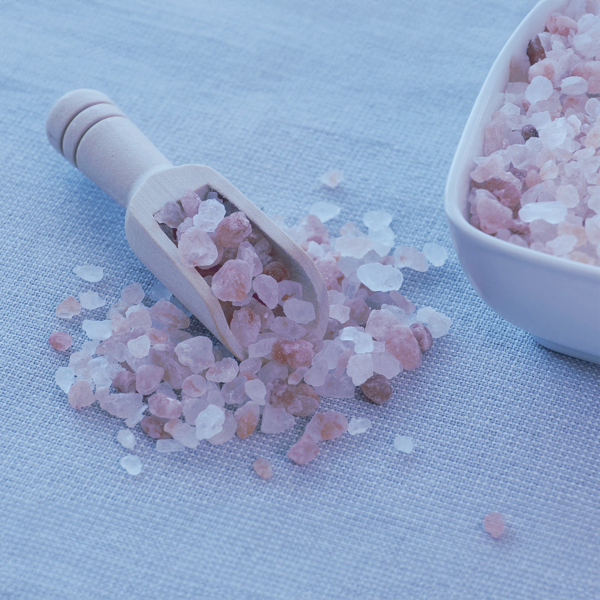 Himalayan Sea Salt Chunks on a linen cloth.  There is a scoop with some of the salt in it and a bowl that has more salt in it as well.