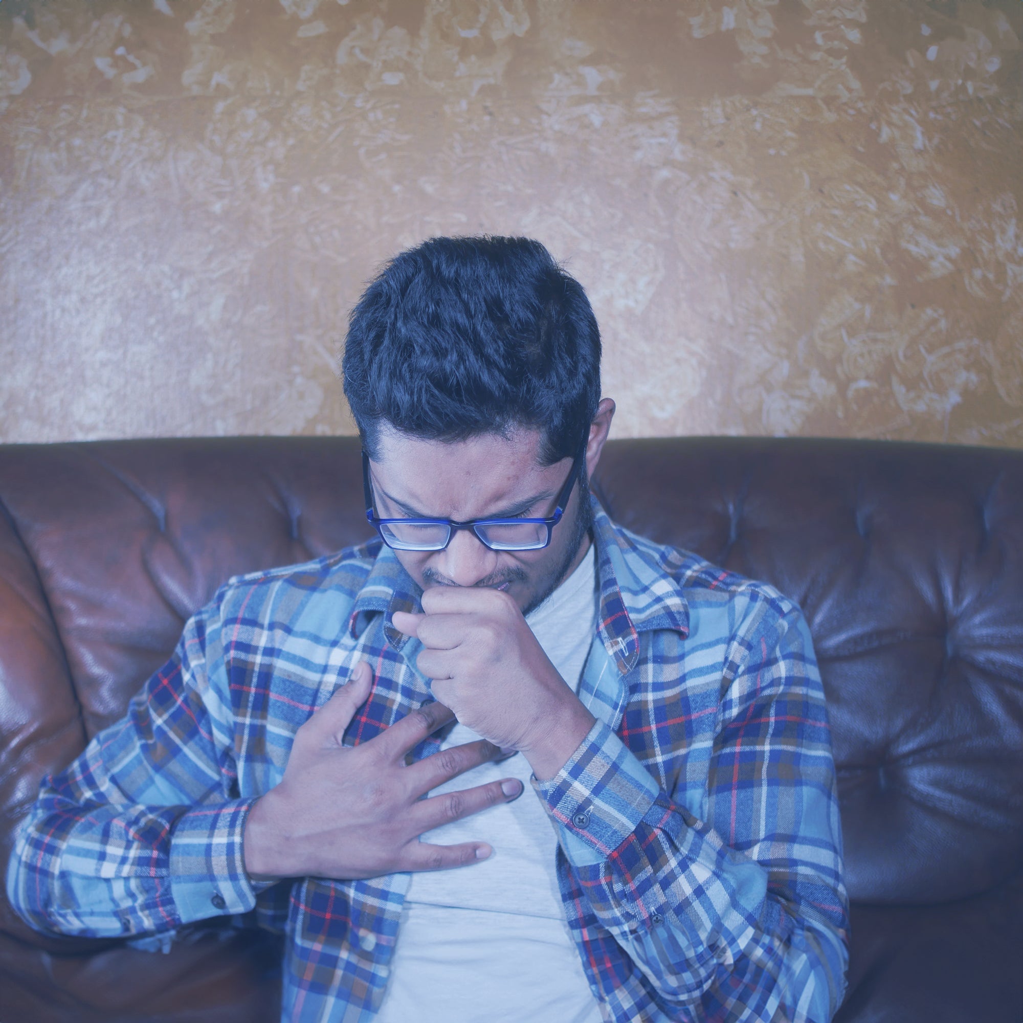 A man, holding his chest with one hand while coughing into the other.