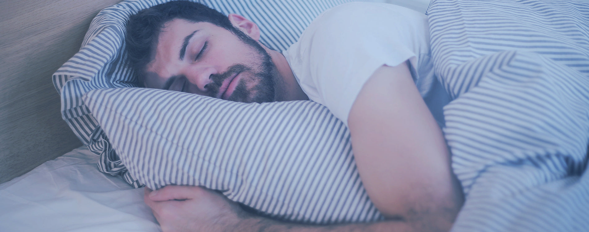 A man with a beard sleeping in bed hugging a pillow