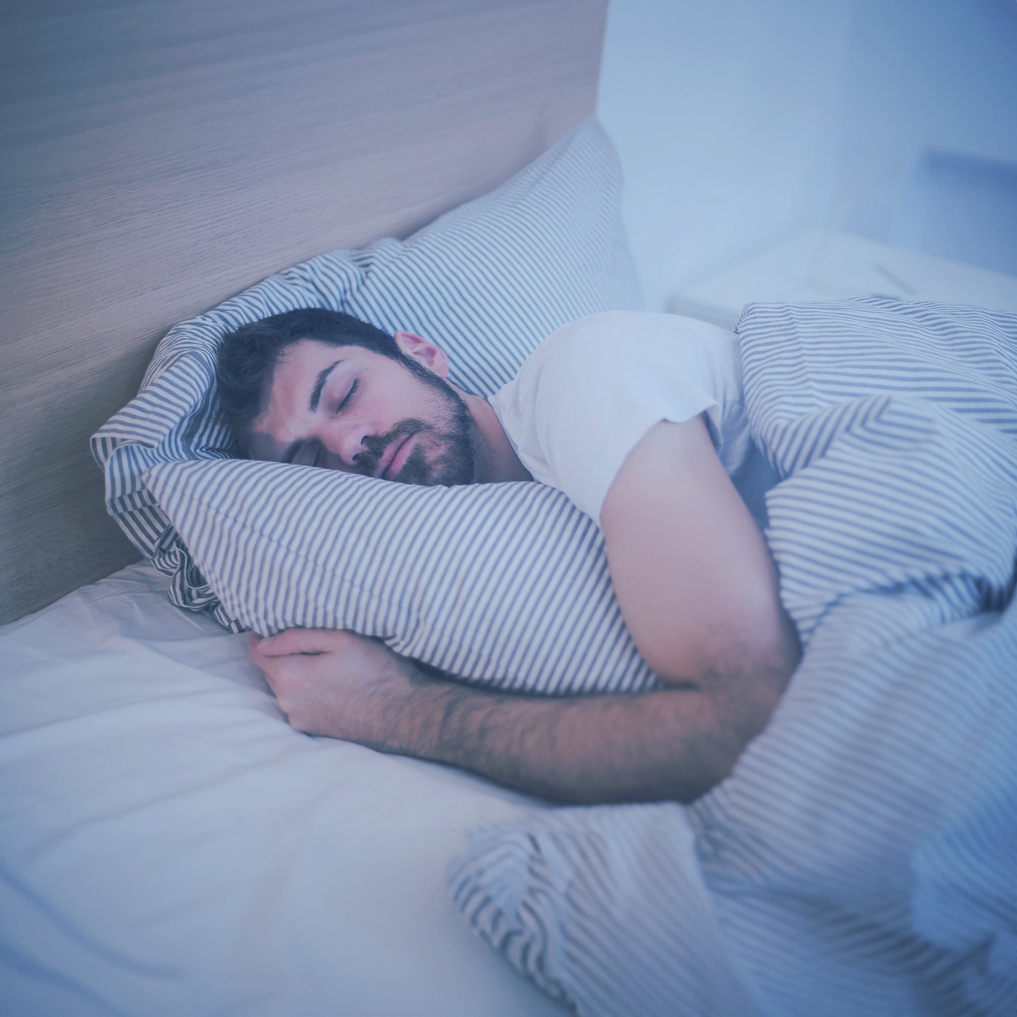 A man with a beard sleeping in bed hugging a pillow