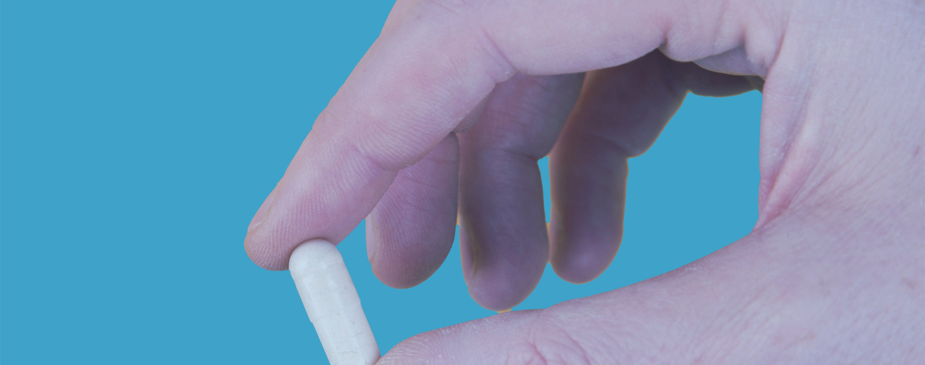 Person's hand holding a single pill of medication or a vitamin