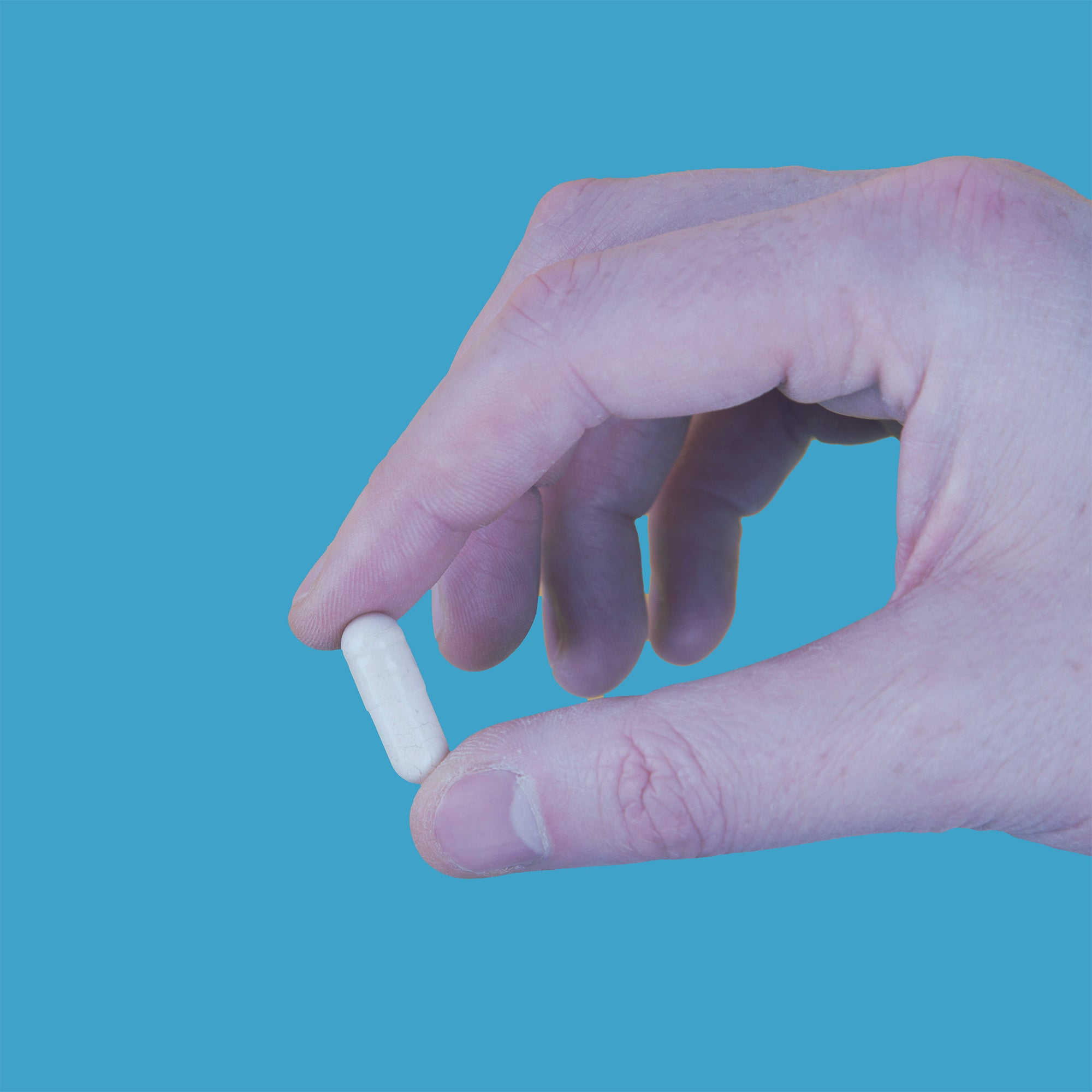 Person's hand holding a single pill of medication or a vitamin