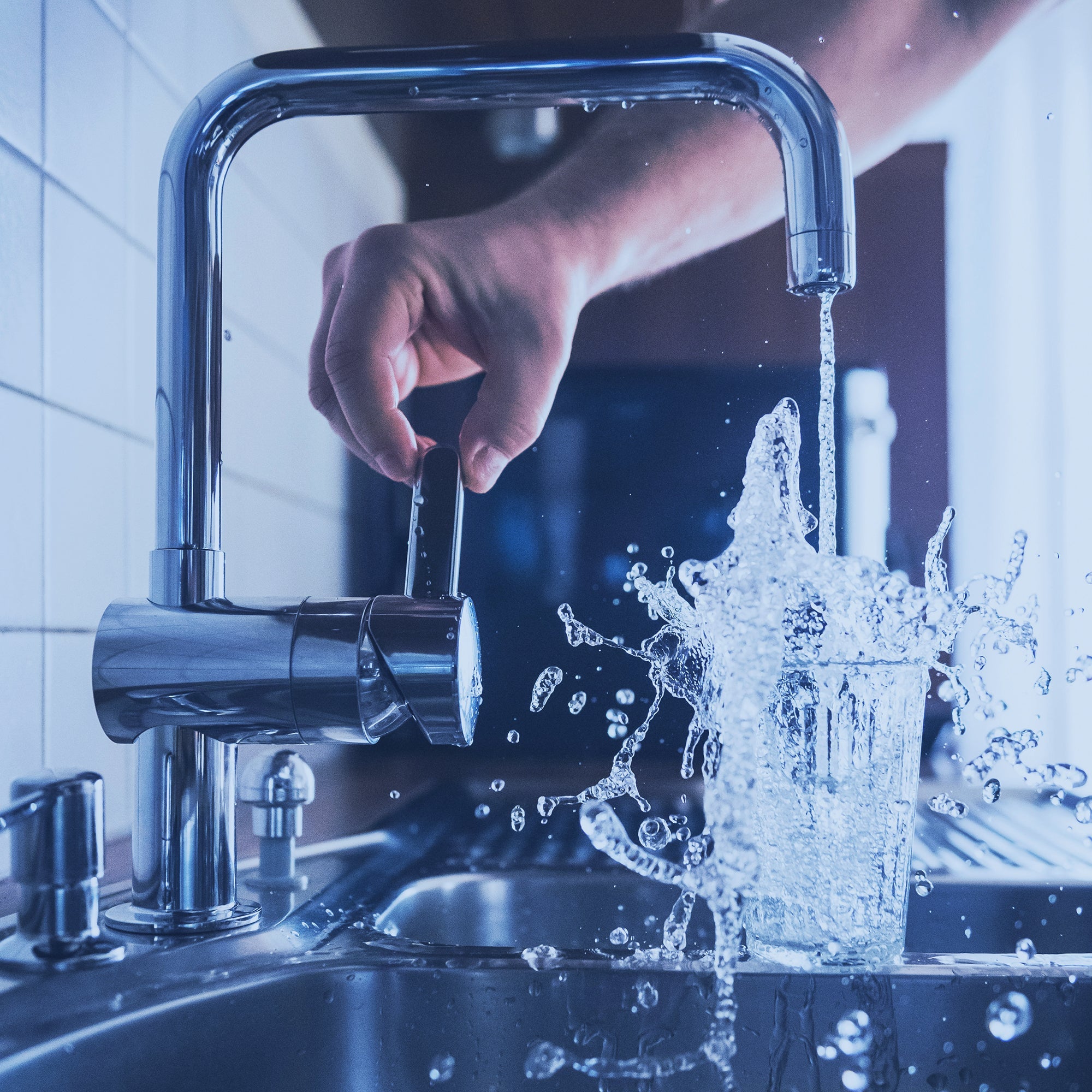 What looks like a fellows hand turning on a sink to fill up a glass of water. The water is splashing out of the glass.