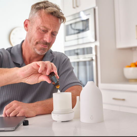 Man in a kitchen pouring a drops of RevitaZen Detpox Blend into a white diffuser