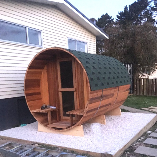Wooden barrel-shaped structure with a green roof in a backyard setting.