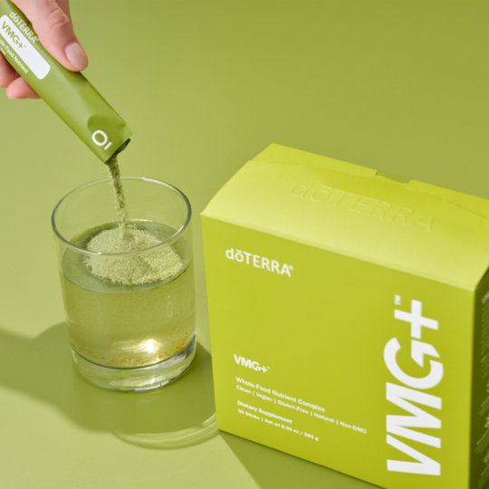 doTERRA VMG+ supplement being added to a glass with a green background